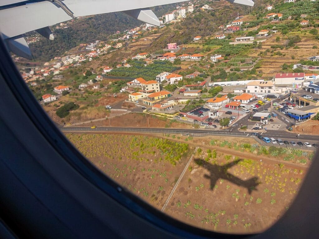 Blick aus dem Flugzeugfenster auf eine Kleinstadt und den Schatten des Flugzeuges