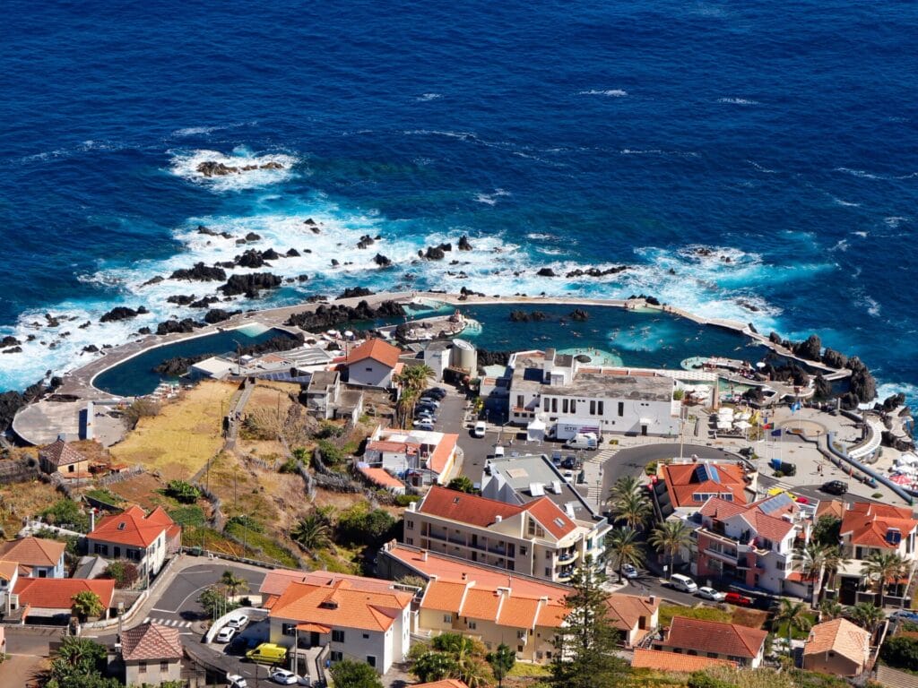 Luftaufnahme einer Kleinstadt an der Meeresküste mit Schutzwällen, die einen Lavapool bilden.