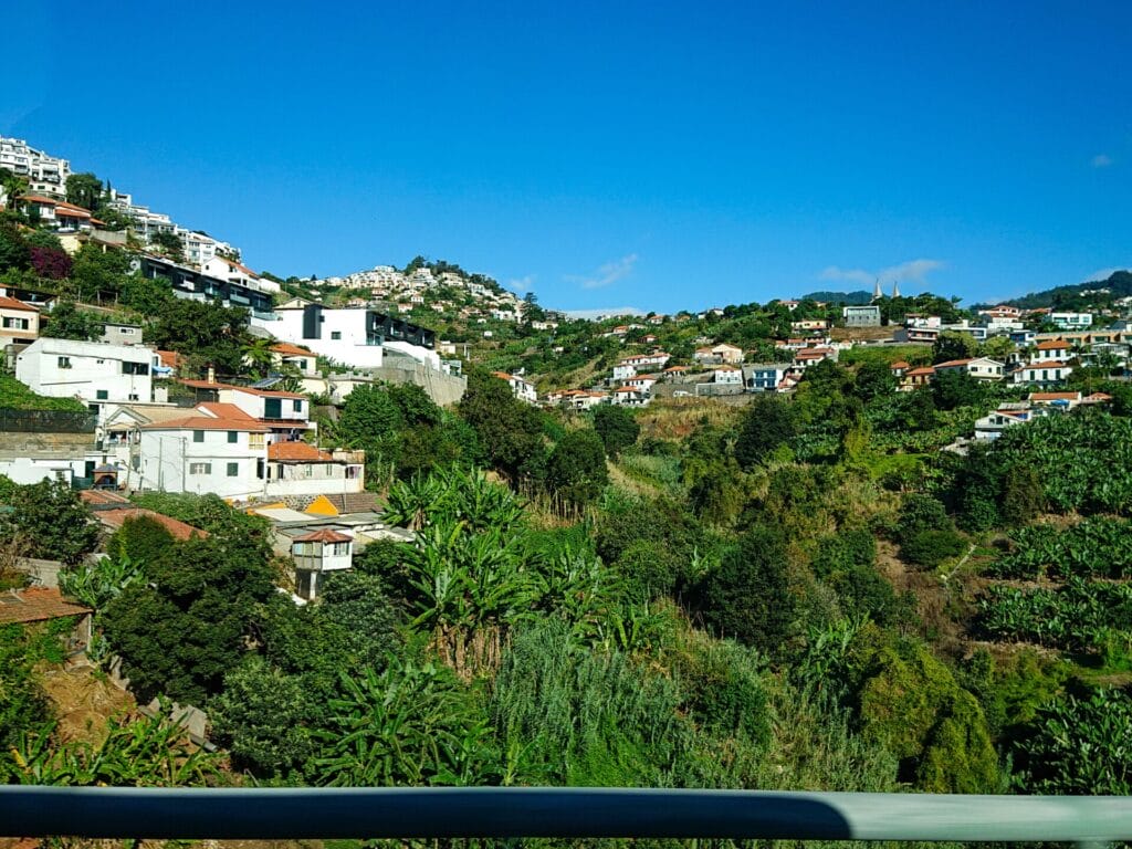 Ausblick vom Reisebus auf grüne Terassenfelder und ein Dorf mit weissen Häusern bei wolkenlosem Himmel